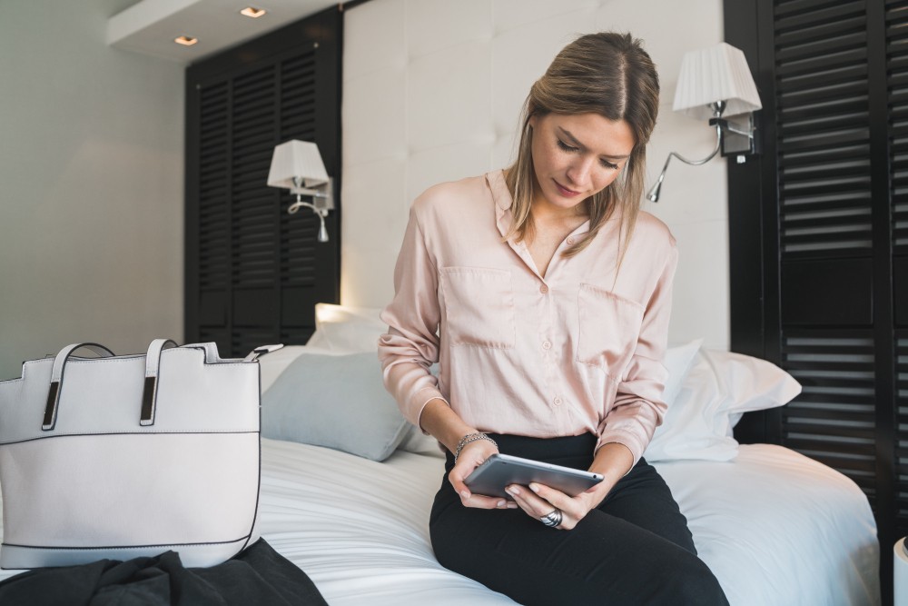 Mulher sentada em uma cama de Airbnb enquanto lê avaliações online.